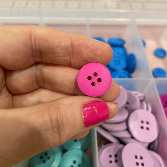 Hand holding a pink button with a container of colorful buttons in the background