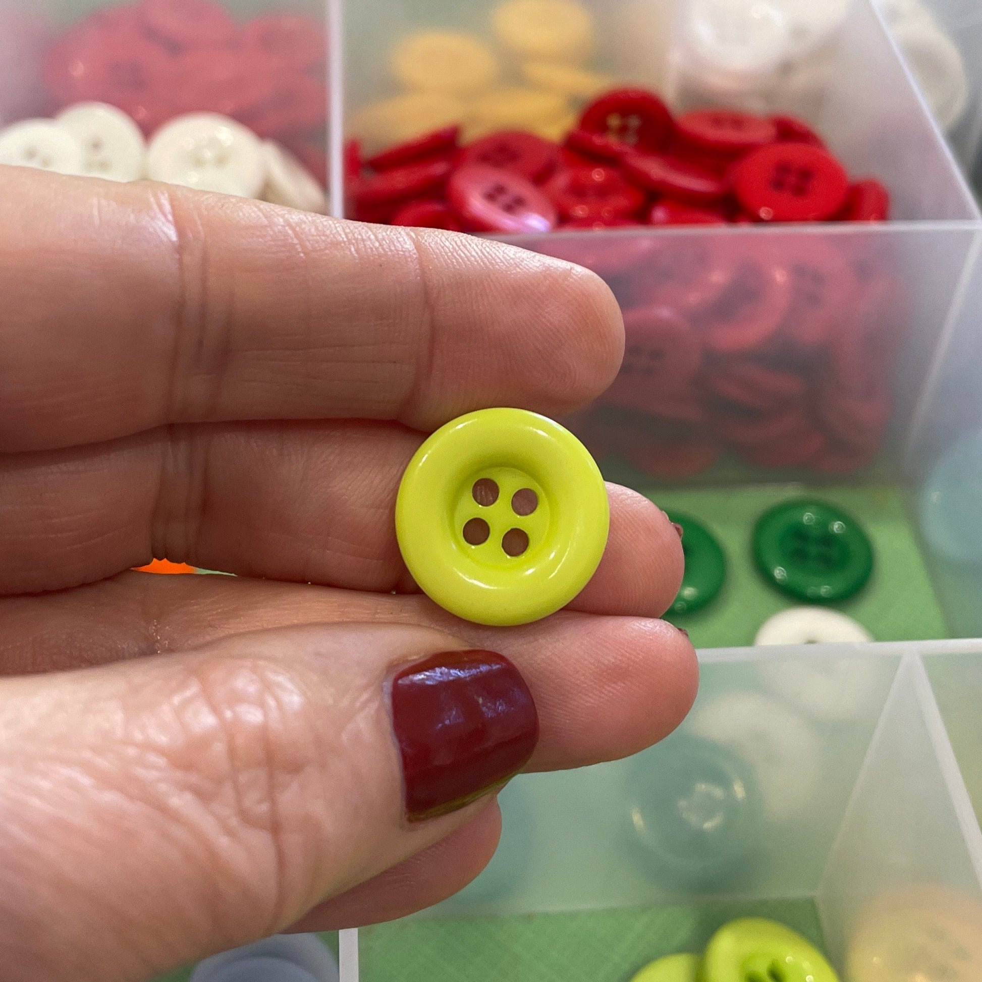Hand holding a yellow button with a background of button containers.