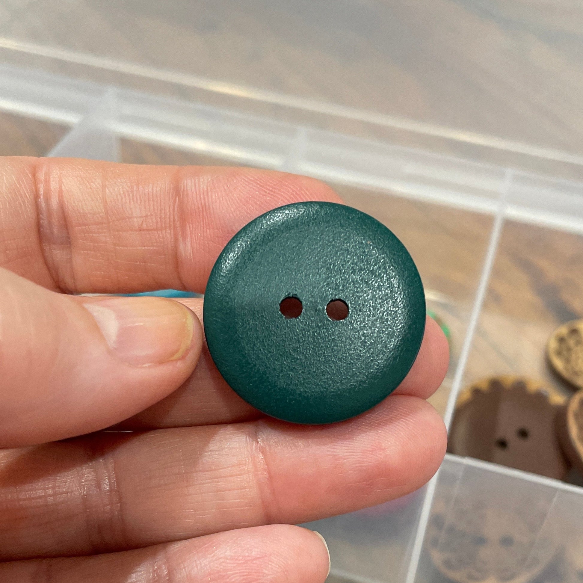 Hand holding a green button with a container of various buttons in the background