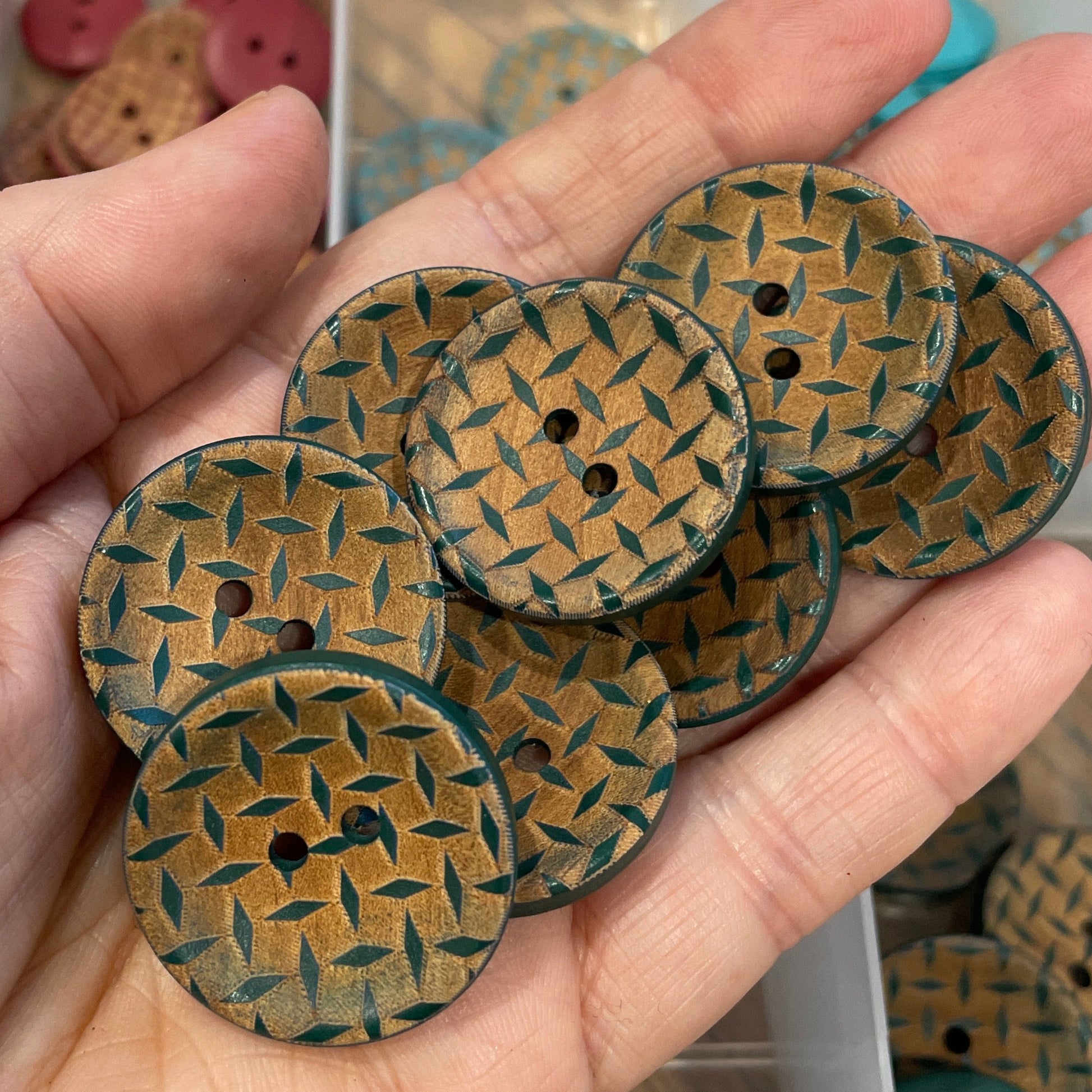 Hand holding woven patterned buttons with a container of buttons in the background.