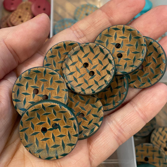 Hand holding woven patterned buttons with a container of buttons in the background.