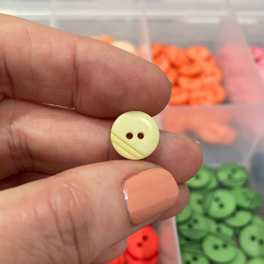 Hand holding a yellow button with a blurred container of buttons in the background