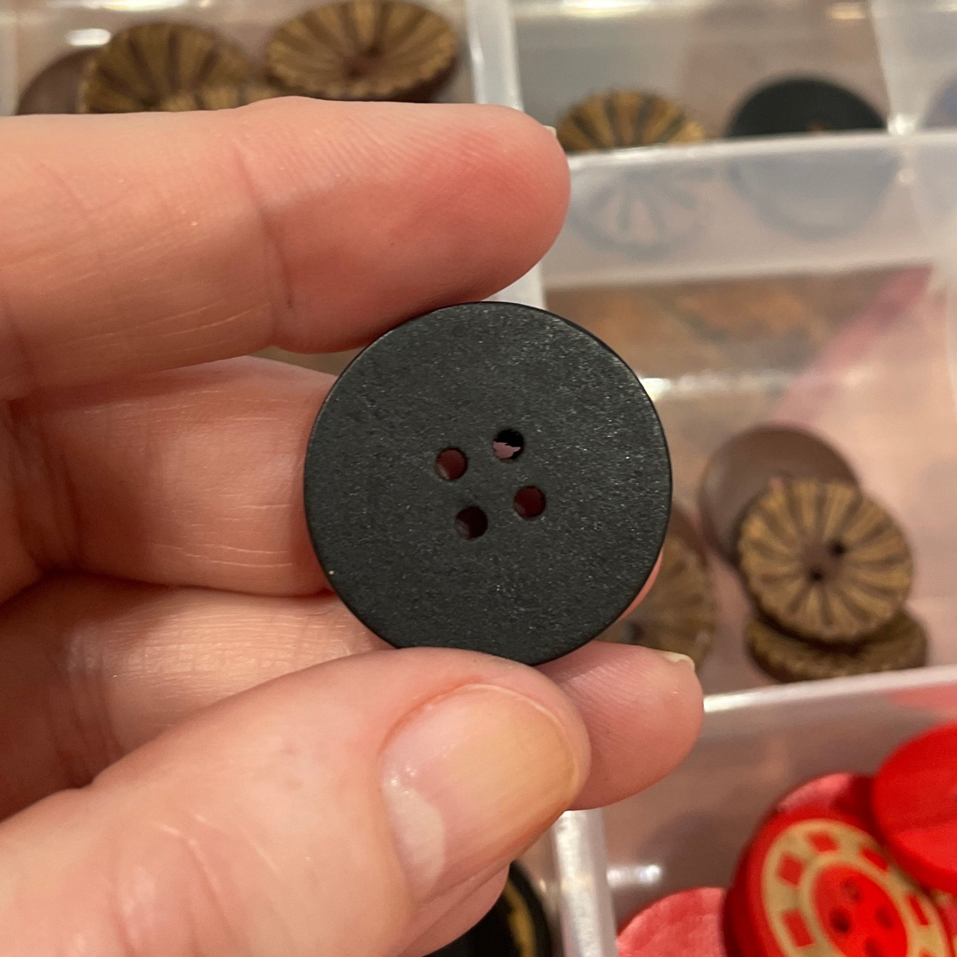 Hand holding a black button with a clear container of buttons in the background