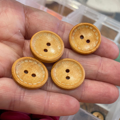 Hand holding yellow buttons with a container of buttons in the background