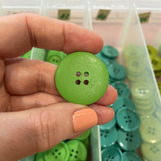 Hand holding a green button with a container of buttons in the background