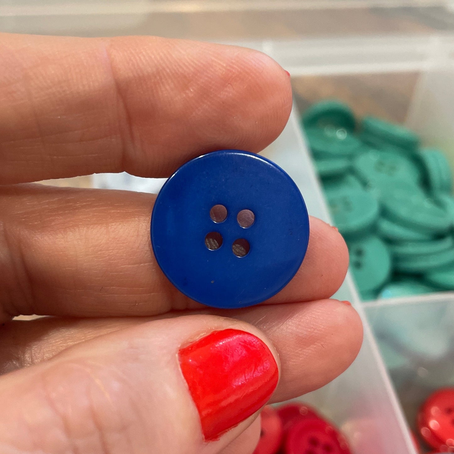 Hand holding a blue button with a container of colorful buttons in the background