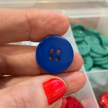 Hand holding a blue button with a container of colorful buttons in the background