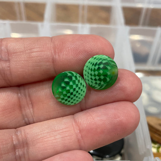 Green textured buttons held between fingers with a button collection in the background