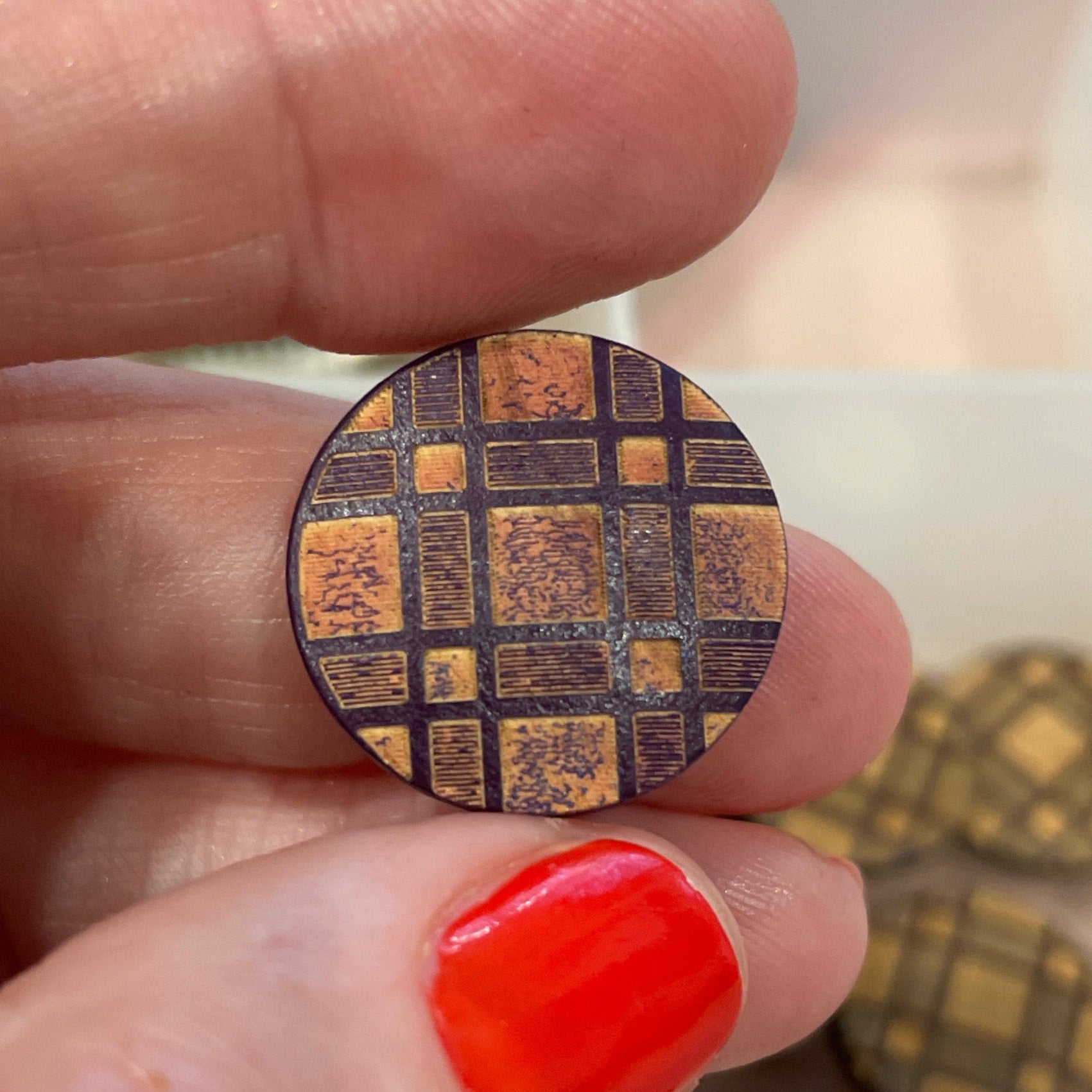 Close-up of a hand holding a circular metallic object with a pattern, against a background of various buttons.