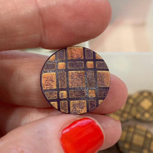 Close-up of a hand holding a circular metallic object with a pattern, against a background of various buttons.