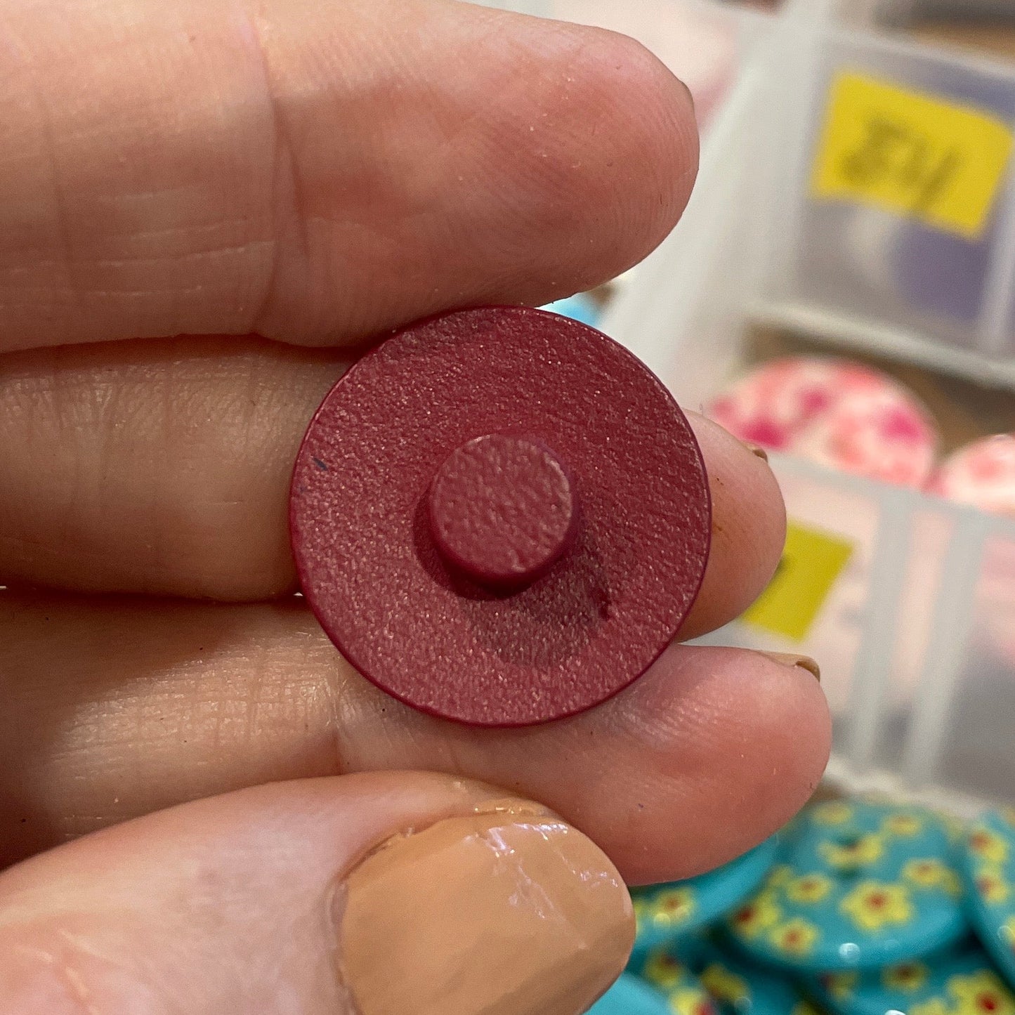 Person holding a red circular object with a blurred background of a storage box with buttons.