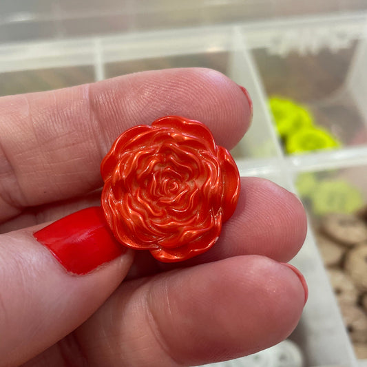 Hand holding a red rose-shaped object with a blurred background of button containers.