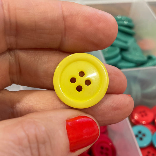 Hand holding a yellow button with a container of red and multicolored buttons in the background