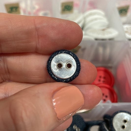 Small black and silver wheel held between fingers with a blurred background of buttons.