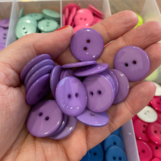 Hand holding purple buttons with a background of colorful buttons in a container.
