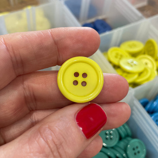 Hand holding a yellow button with a container of colorful buttons in the background