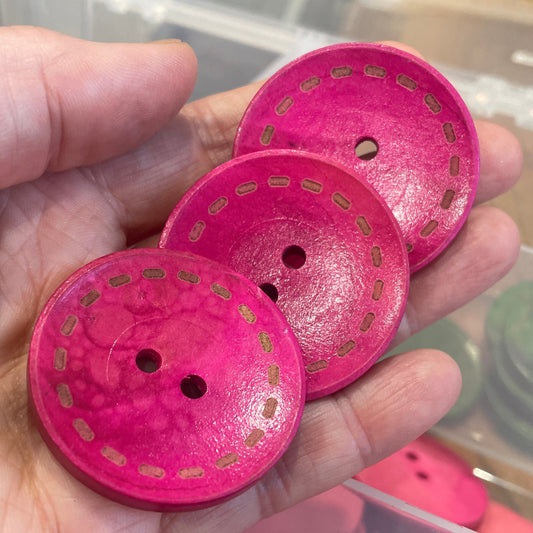 Hand holding pink buttons with a clear container of more buttons in the background