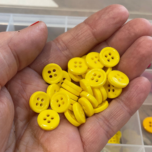 Hand holding yellow buttons with a container of buttons in the background