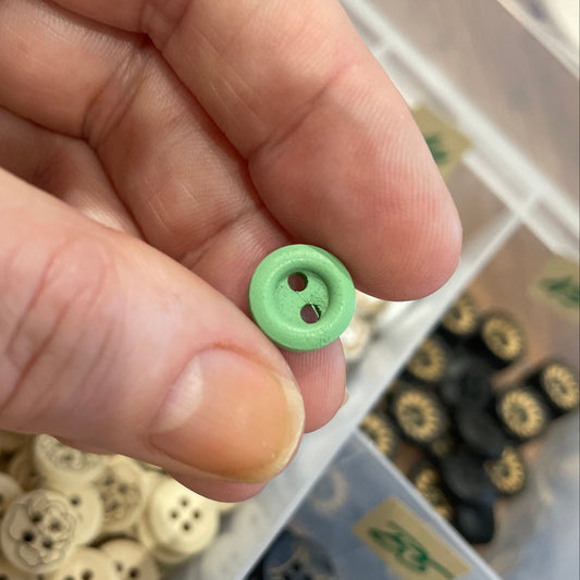 Hand holding a green button with a container of buttons in the background