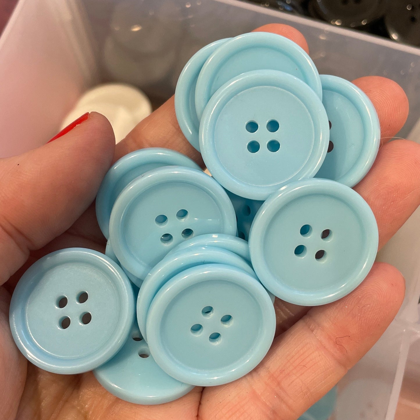 Hand holding light blue buttons with a container of assorted buttons in the background
