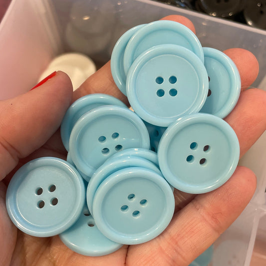 Hand holding light blue buttons with a container of assorted buttons in the background