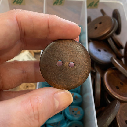 Hand holding a brown button with a container of buttons in the background