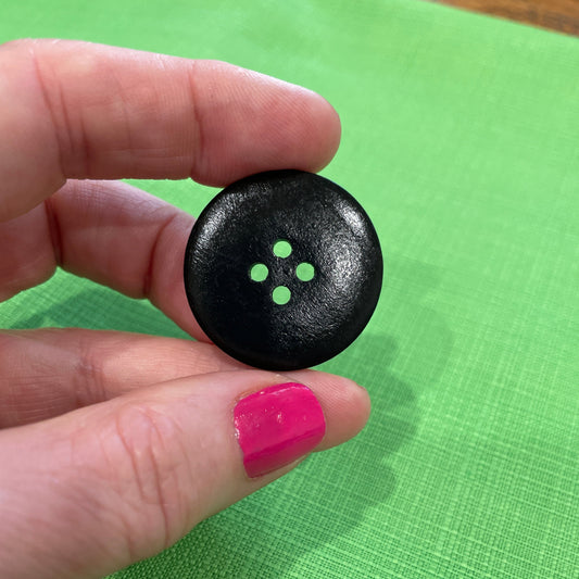 Black button held between fingers against a green fabric background