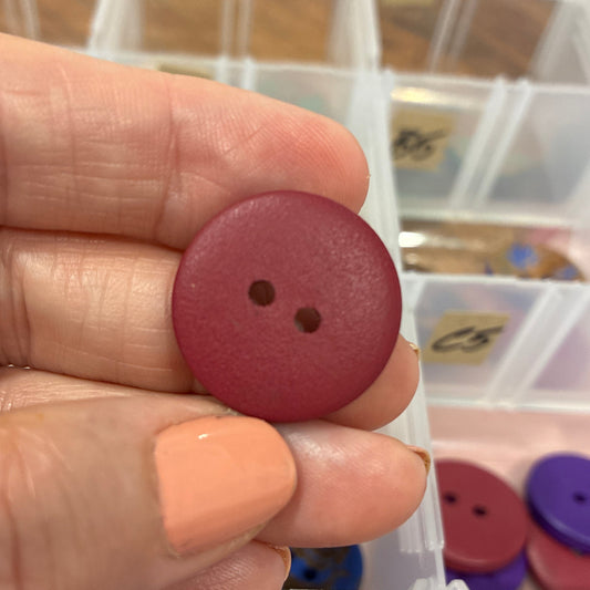 Hand holding a red button with a background of button containers.