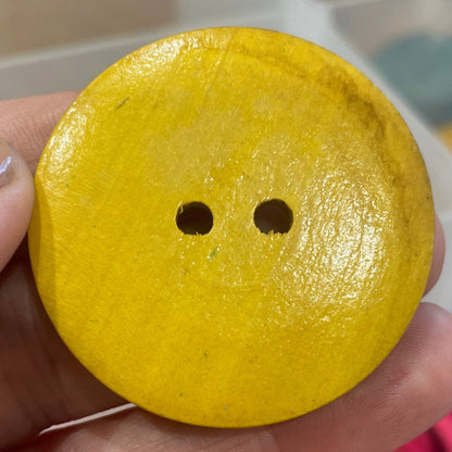 Yellow button held by a hand with pink buttons in the background