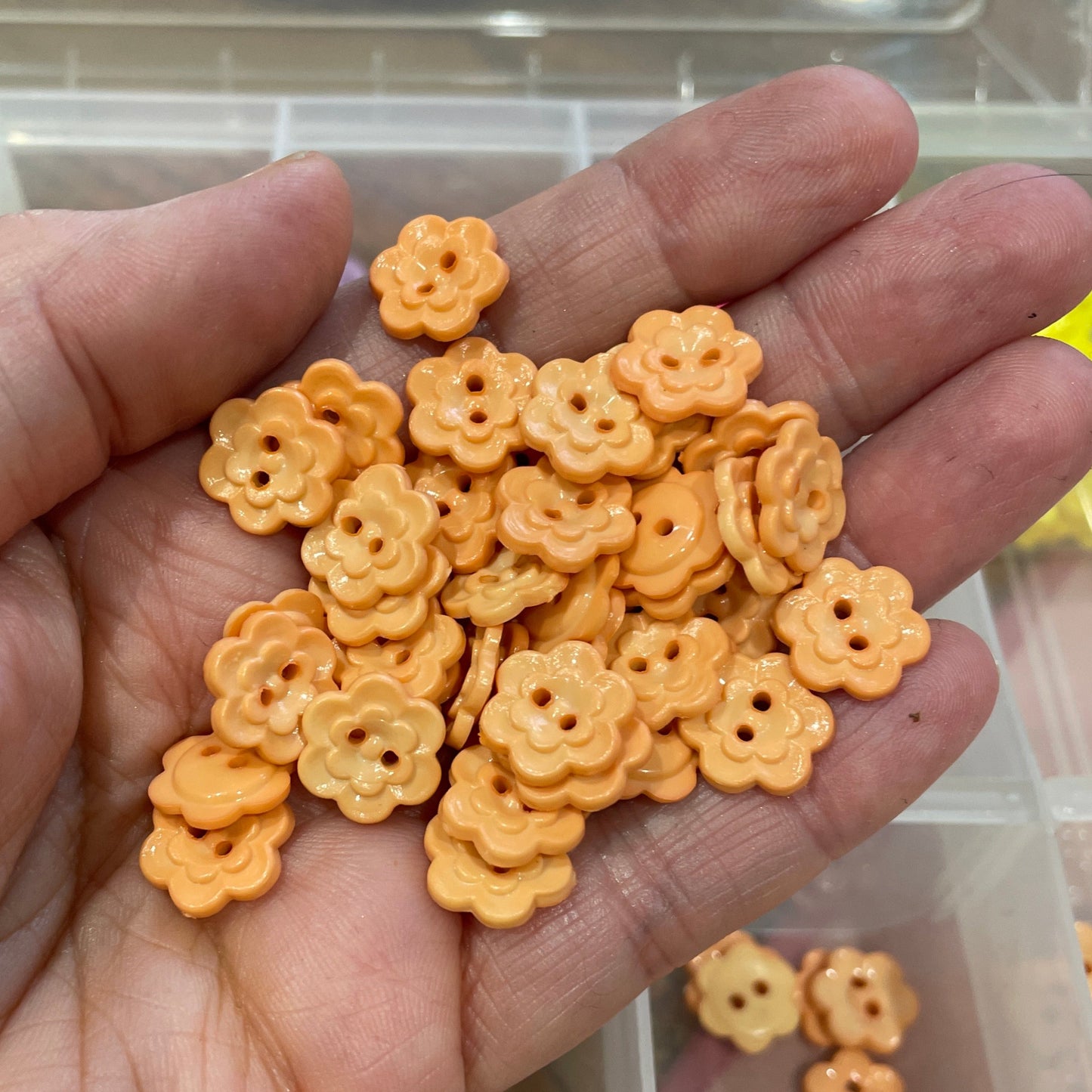 Hand holding small orange floral-shaped objects with a container of similar objects in the background.