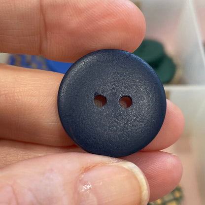 Hand holding a blue button with a blurred background of a button collection.