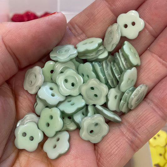 Hand holding green floral buttons with a blurred background of more buttons.