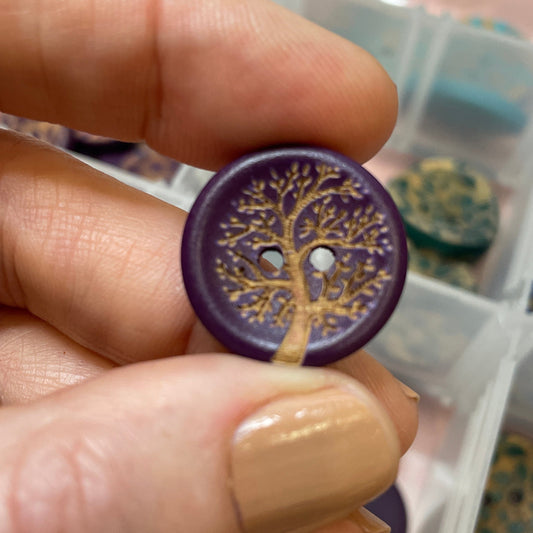 Hand holding a purple button with gold design over a container of buttons.