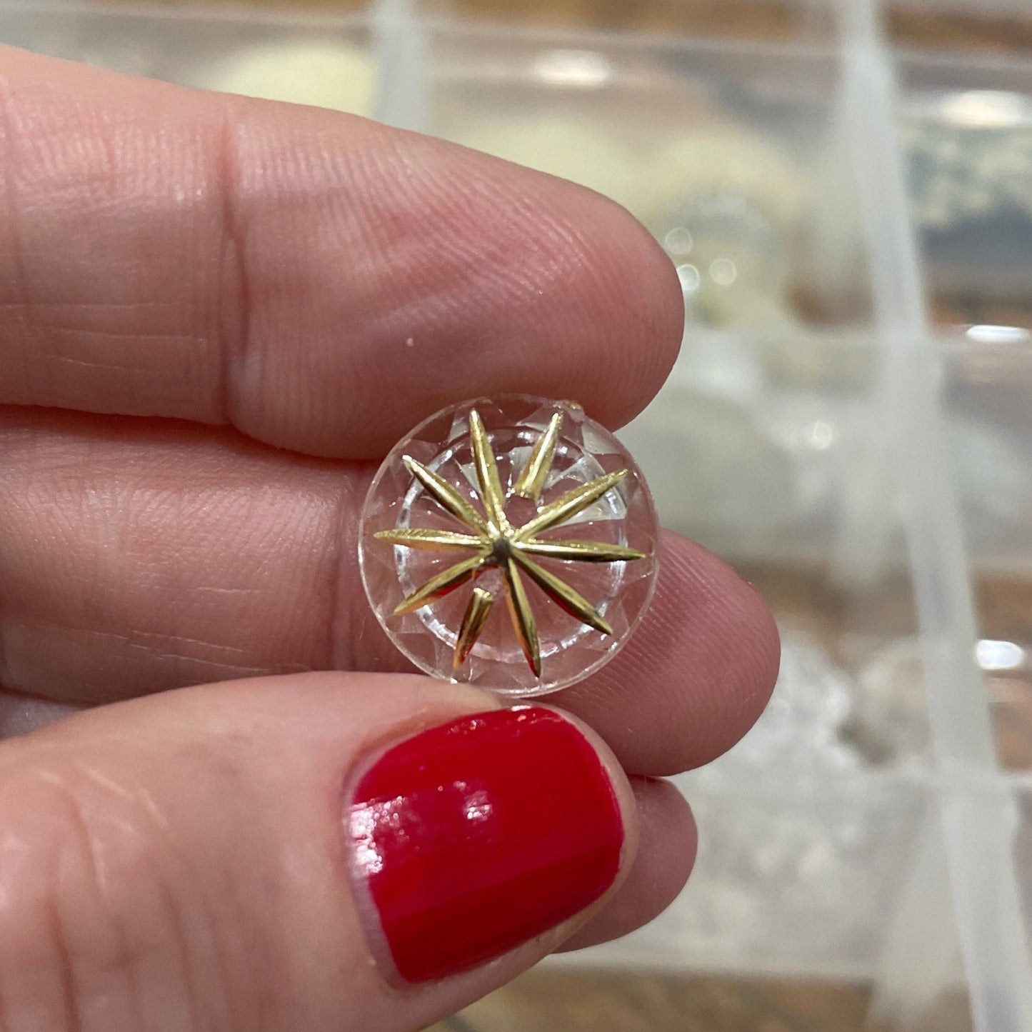 Gold and clear earring held between fingers with a blurred background