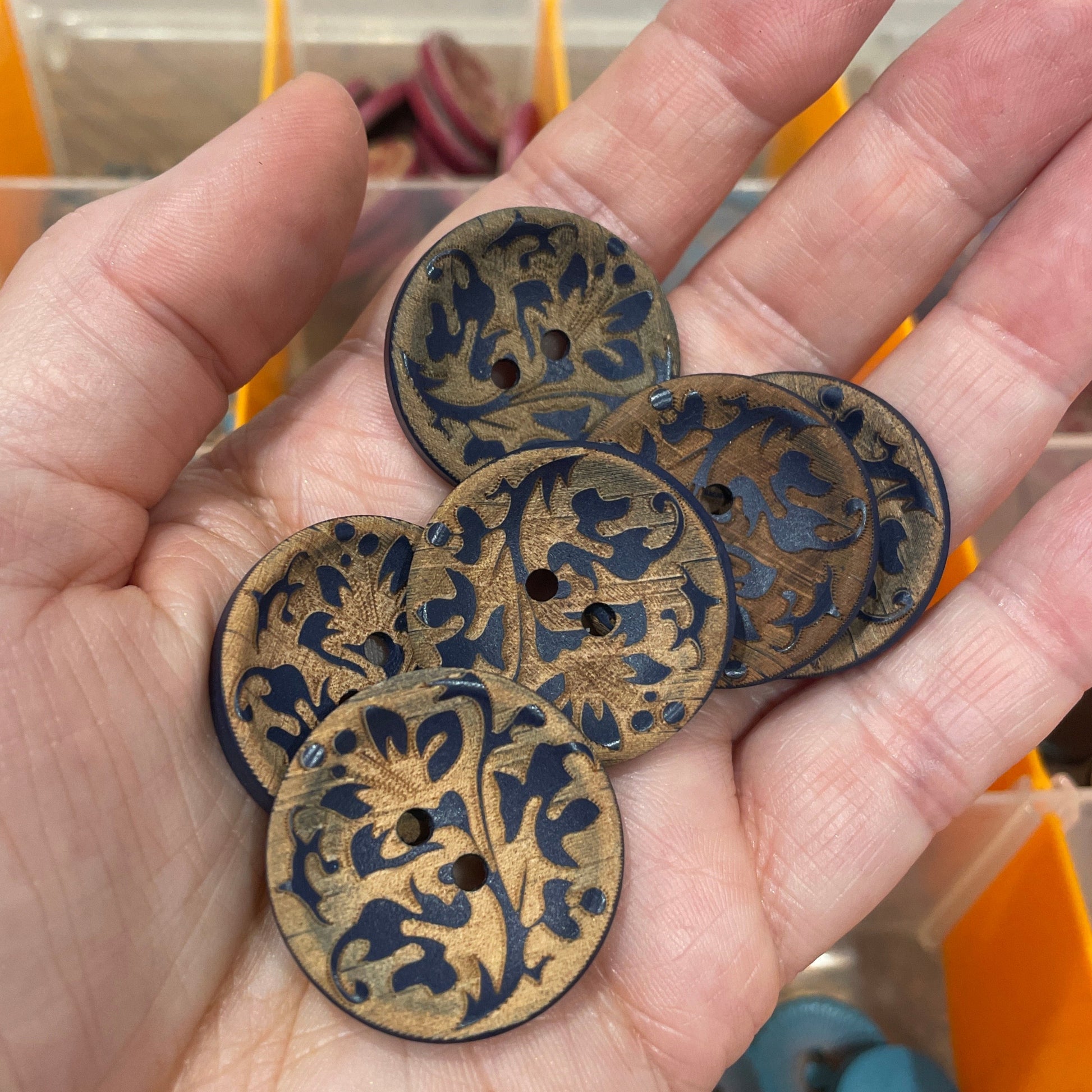 Hand holding three decorative metal discs with intricate designs against a blurred background.