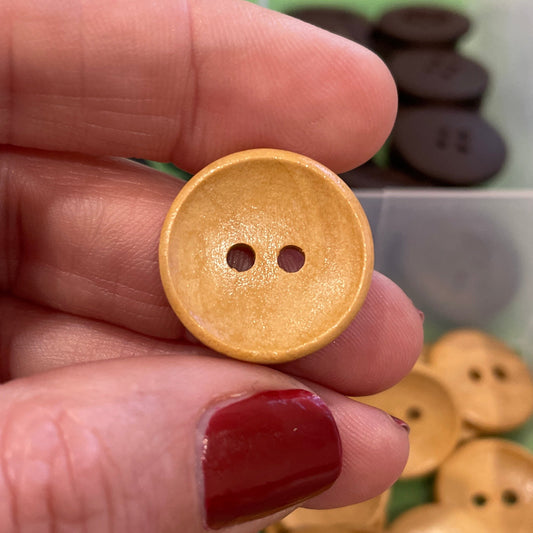 Hand holding a gold button with a clear container of buttons in the background
