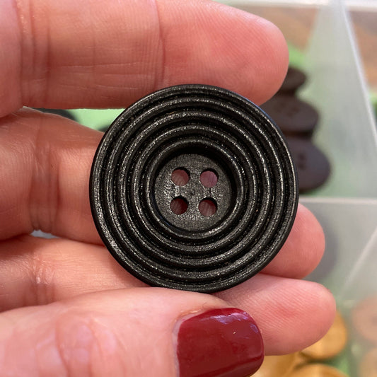 Hand holding a black spiral button with a container of buttons in the background