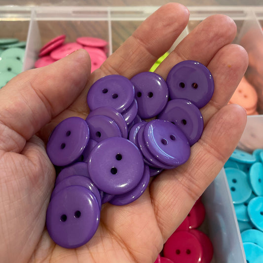 Hand holding purple buttons with a container of colorful buttons in the background