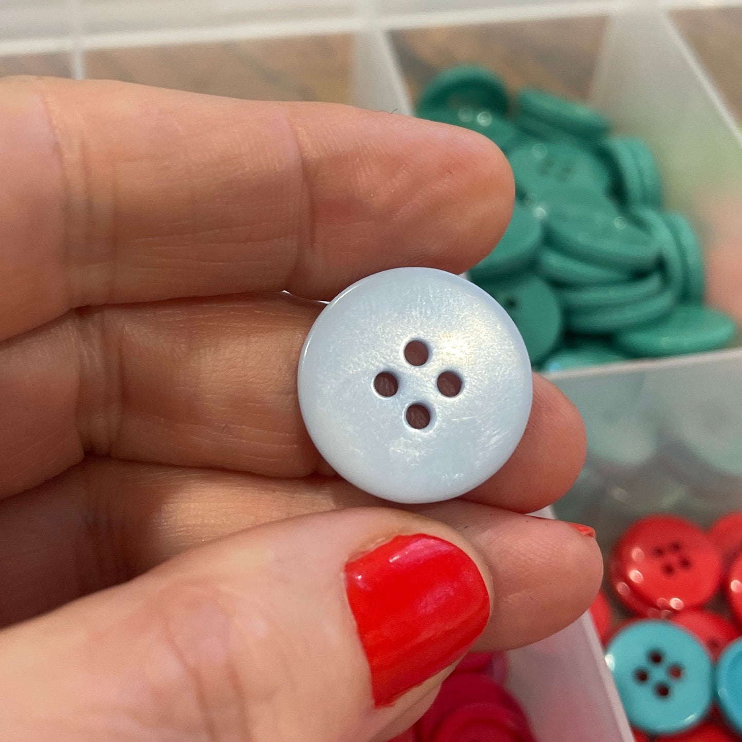 Hand holding a white button with a container of colorful buttons in the background