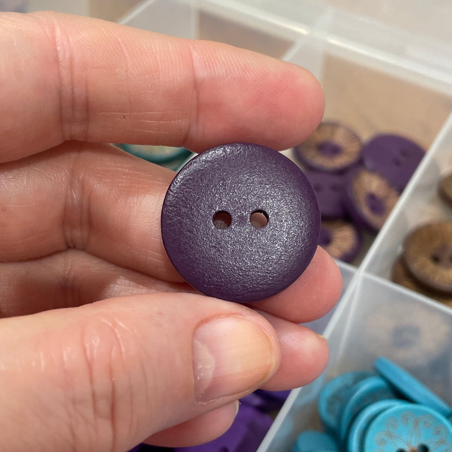 Hand holding a purple button with a container of buttons in the background