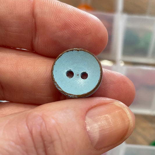 Hand holding a button with a blurred background of a button collection box.