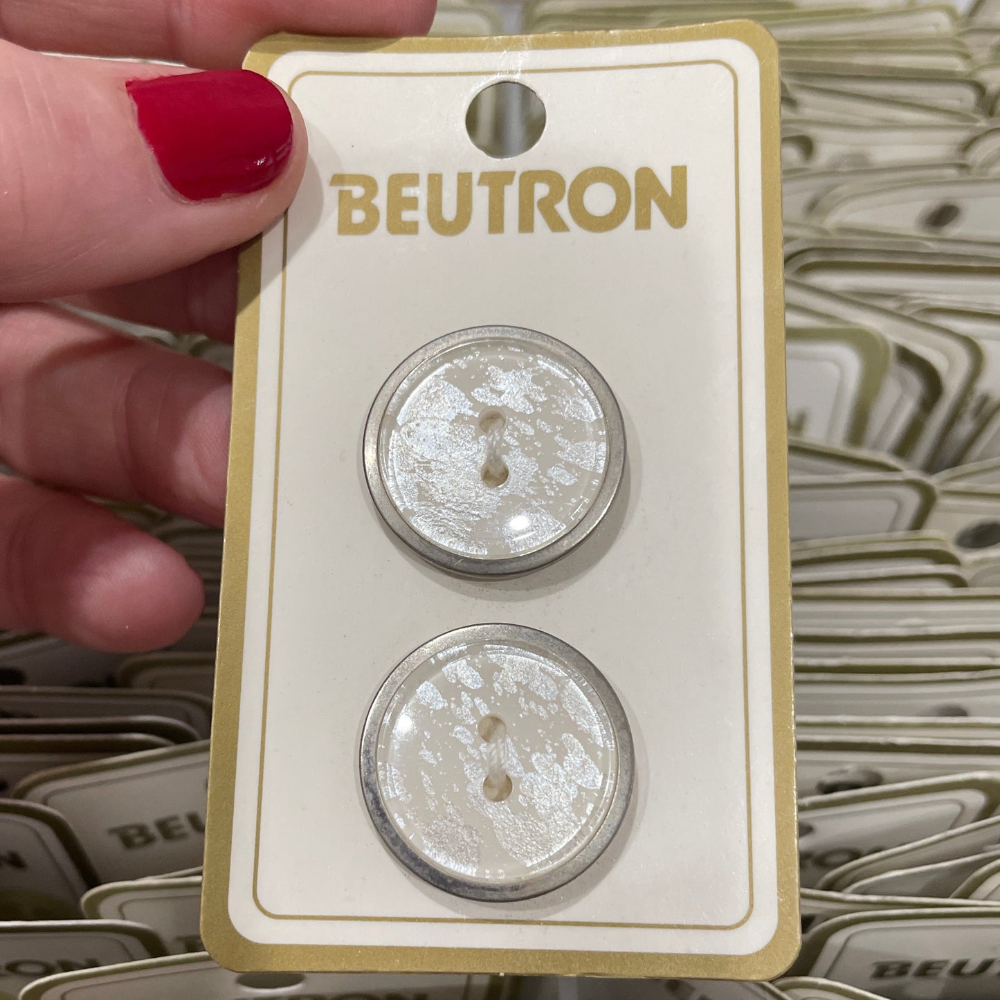Pair of buttons on a BEUTRON card held by a hand with red nail polish.