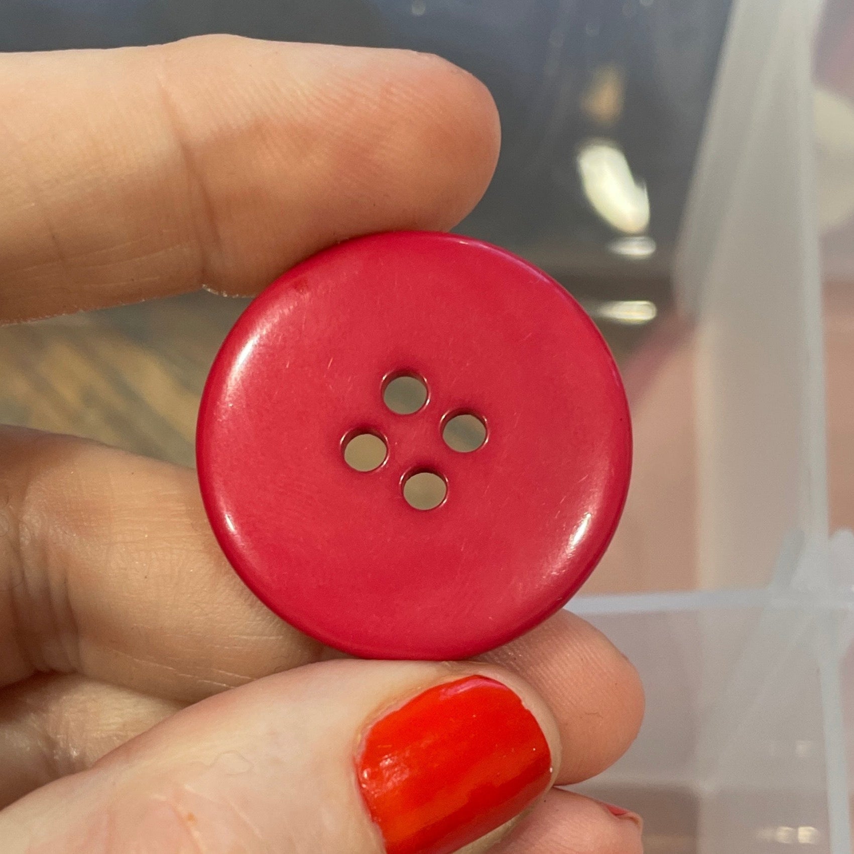 Hand holding a red button with a clear container of buttons in the background