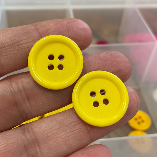 Hand holding two yellow buttons with a clear container of buttons in the background