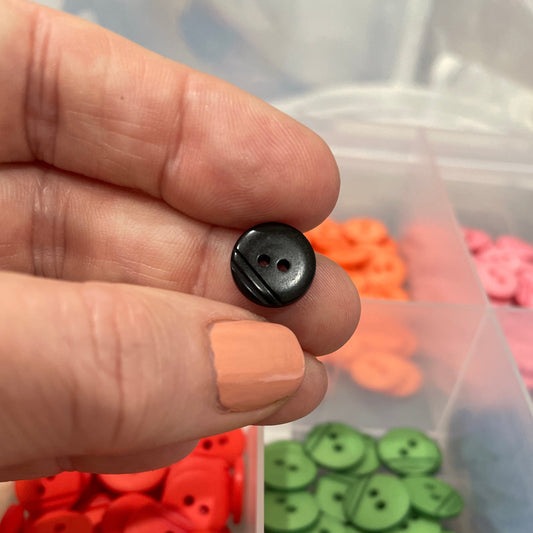 Hand holding a black button with a container of colorful buttons in the background