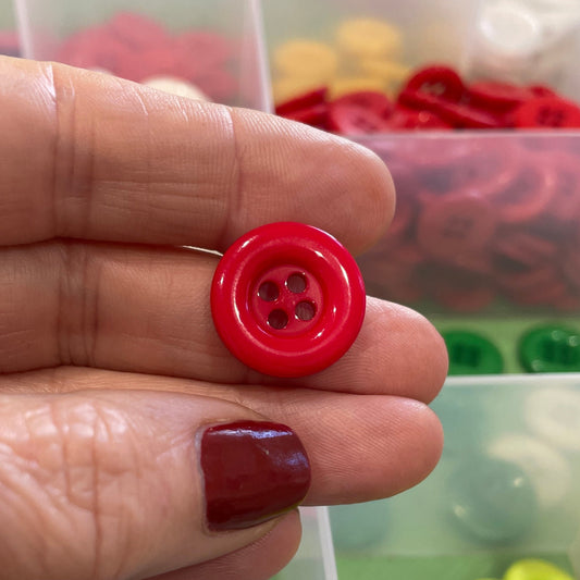 Hand holding a red button with a container of assorted buttons in the background