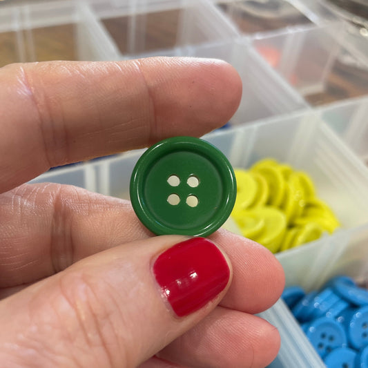 Hand holding a green button with a container of colorful buttons in the background