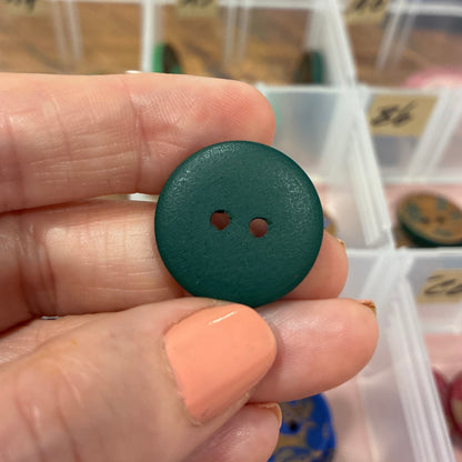 Hand holding a green button with a container of buttons in the background