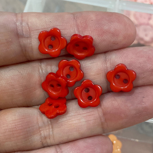 Hand holding red flower-shaped buttons with a container of similar buttons in the background.