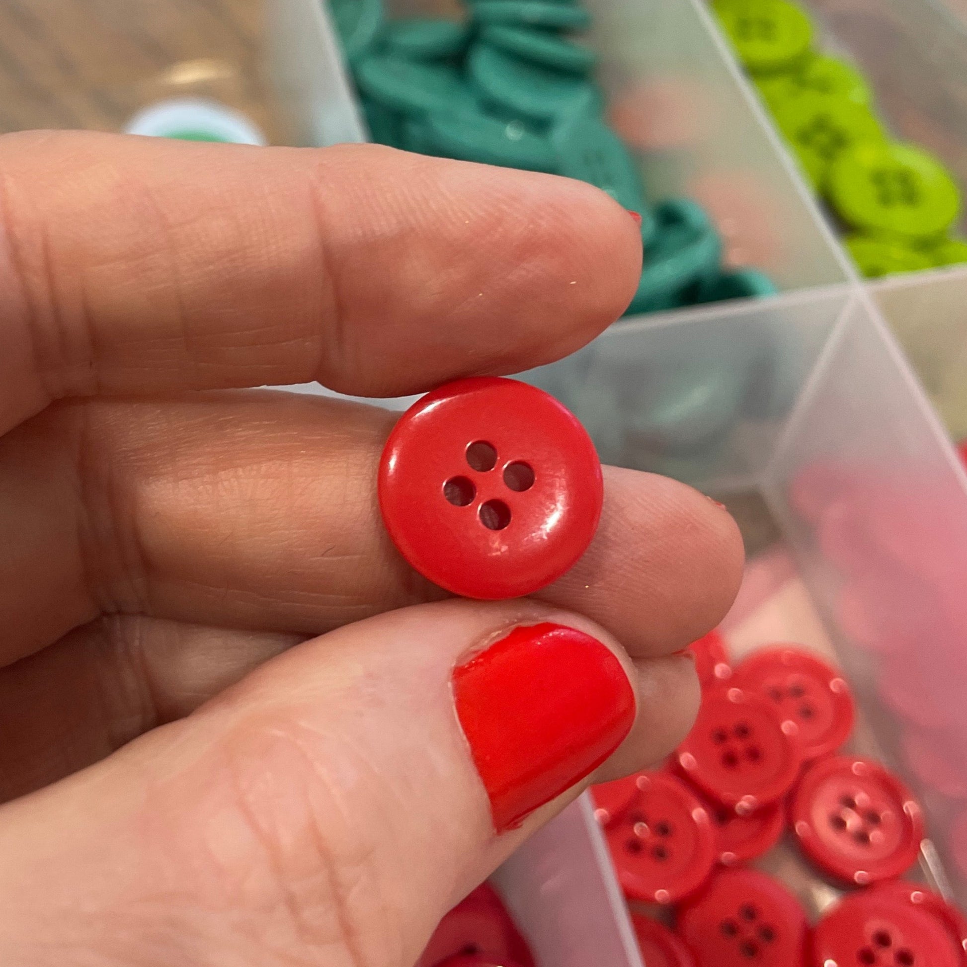 Hand holding two red buttons with a container of assorted buttons in the background